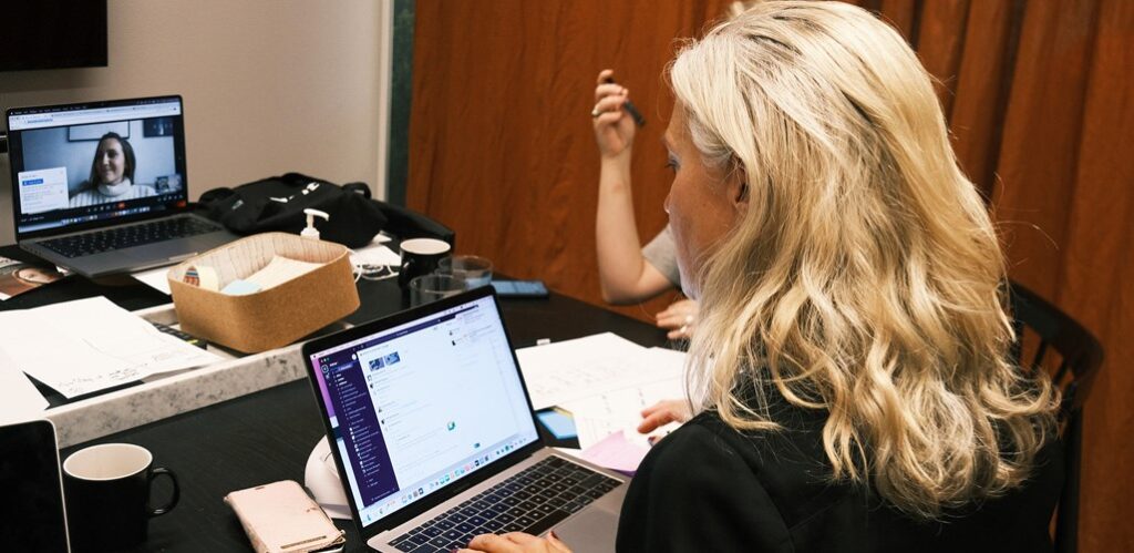 Kvinna tittar in i datorn samtidigt som hon har en annan dator med ett onlinemöte.