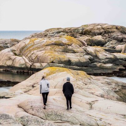Vi ser två personer som promenerar på klipporna i naturen