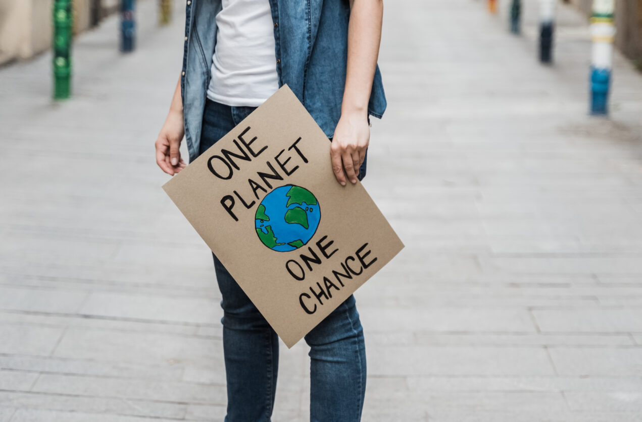 Bild på jeansklädd person som håller i en demonstrationsskylt. På skylten står det One Planet One Chance och ett jordklot är målat på skylten.