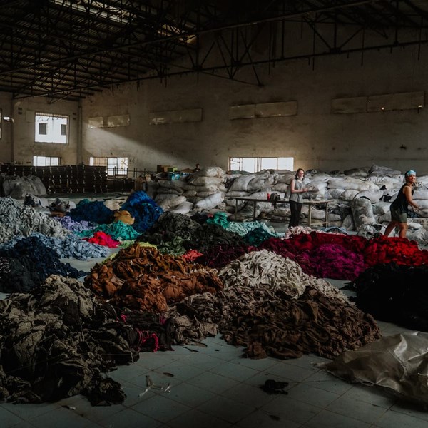 Bild på många högar med kläder på golvet i en stor fabrikslokal.