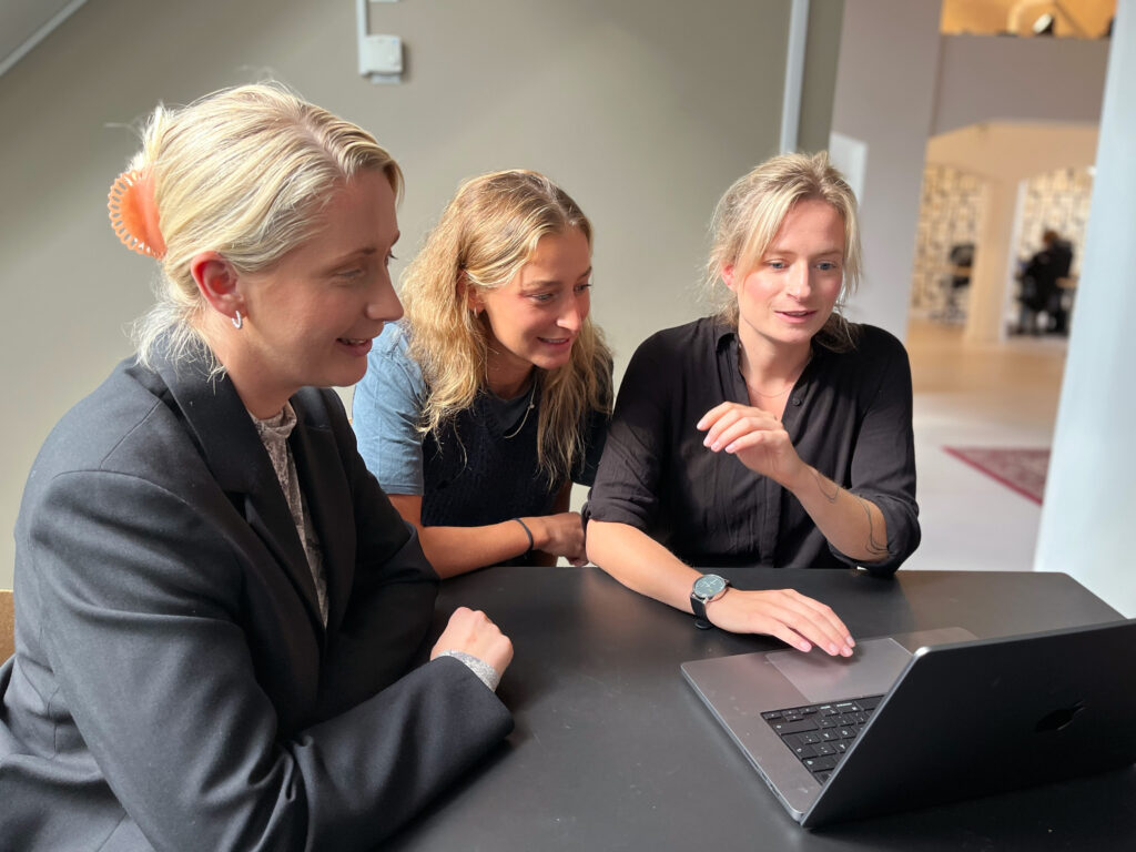 Tre kvinnliga kollegor sitter vid ett bord och kollar på en dator.