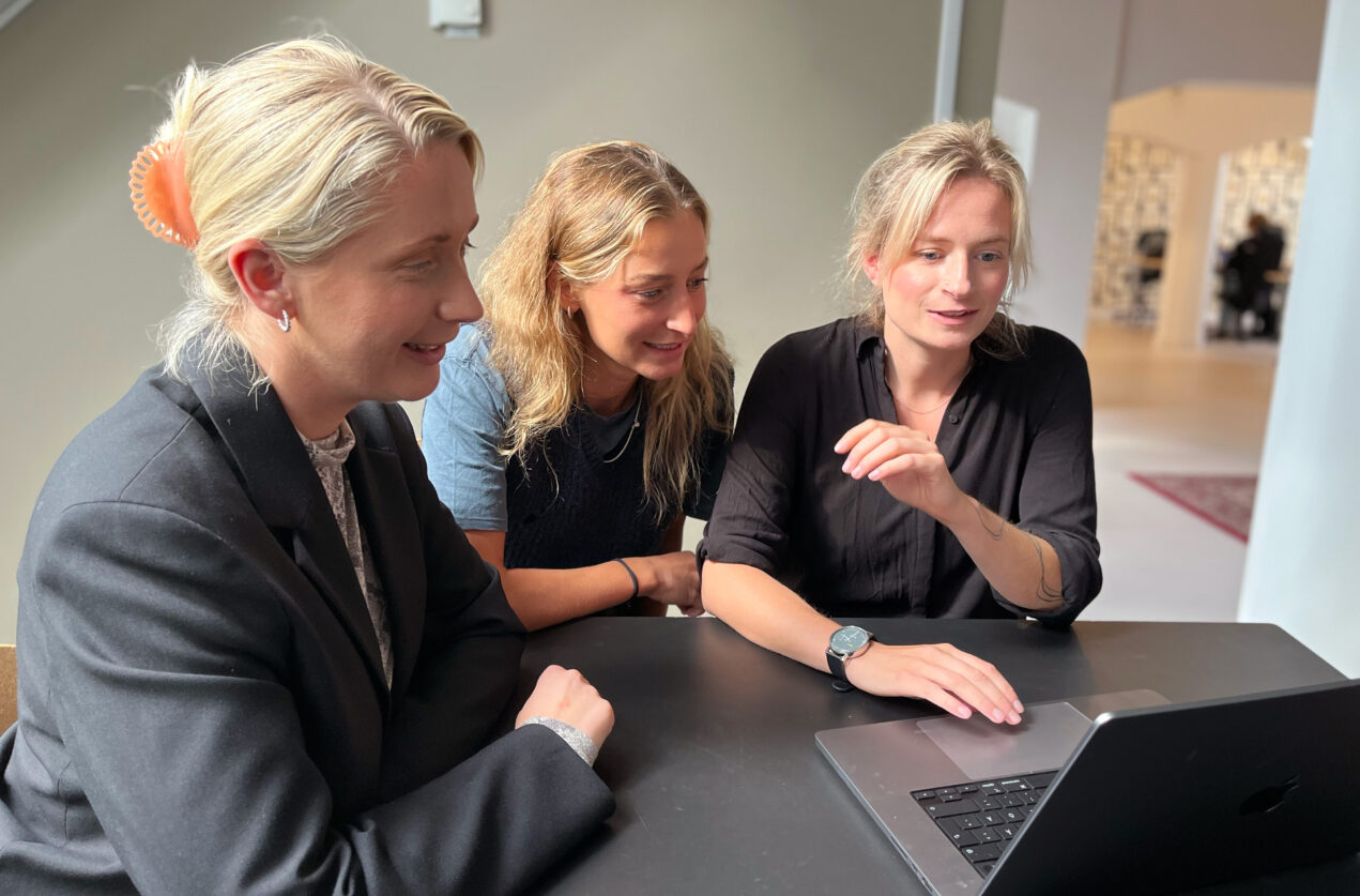 Tre kvinnliga designers tittar på en datorskärm tillsammans för att hjälpa varandra framåt