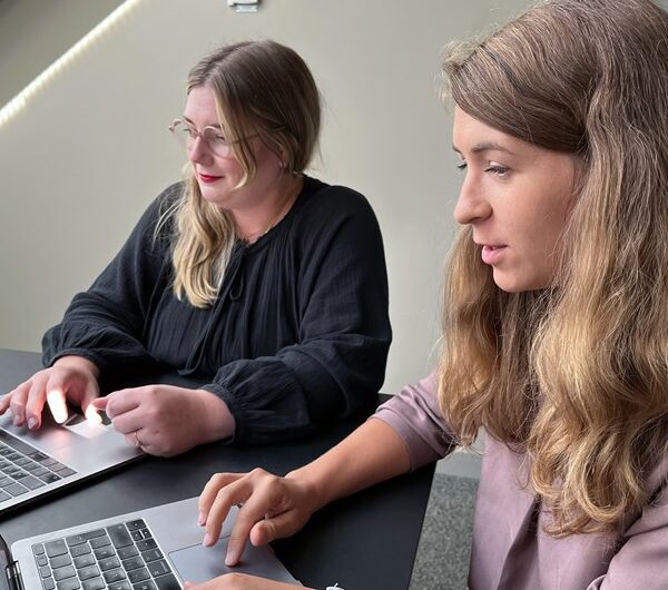 Två kvinnliga kollegor sitter framför varsin dator och jobbar.