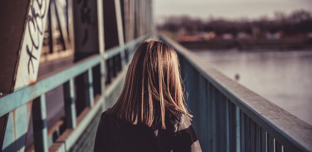 Bild av ung person bakifrån som går ensam på en bro over vatten.