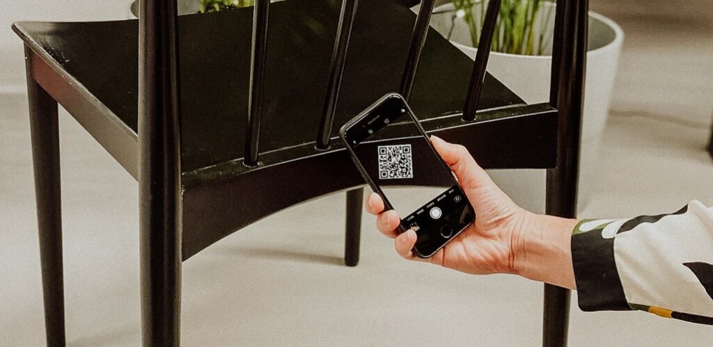Bild på en hand som håller i en telefon och skannar en QR kod på en svart stol.