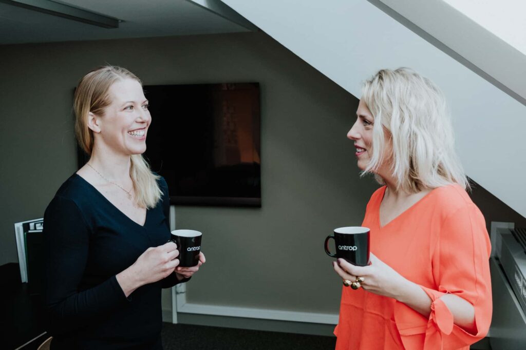 Två kvinnor håller i varsin kaffekopp och ler mot varandra.