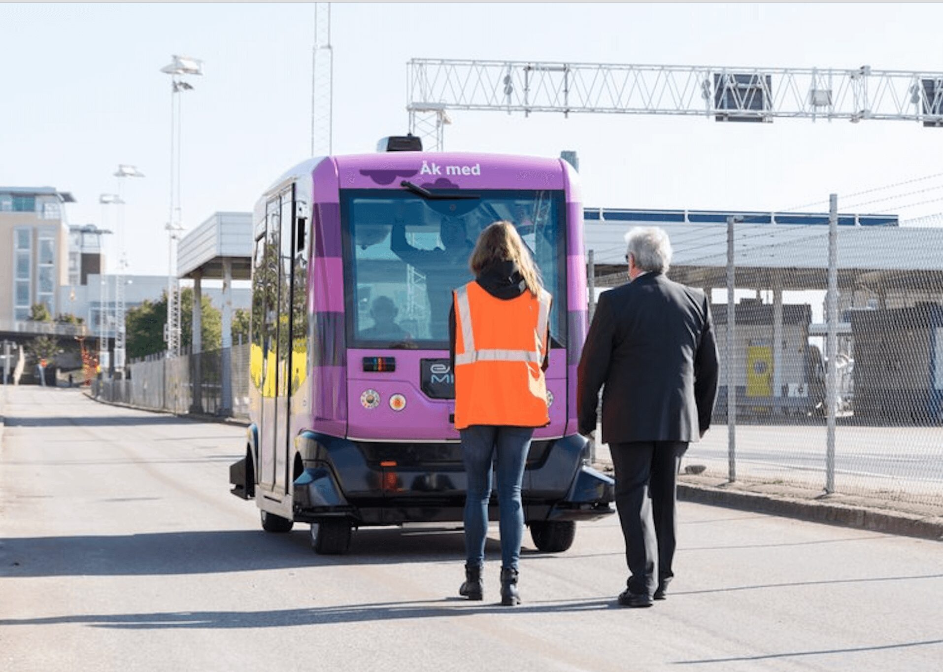 Två personer går mot en liten autonom elbuss med texten "Åk med" i Helsingborg.