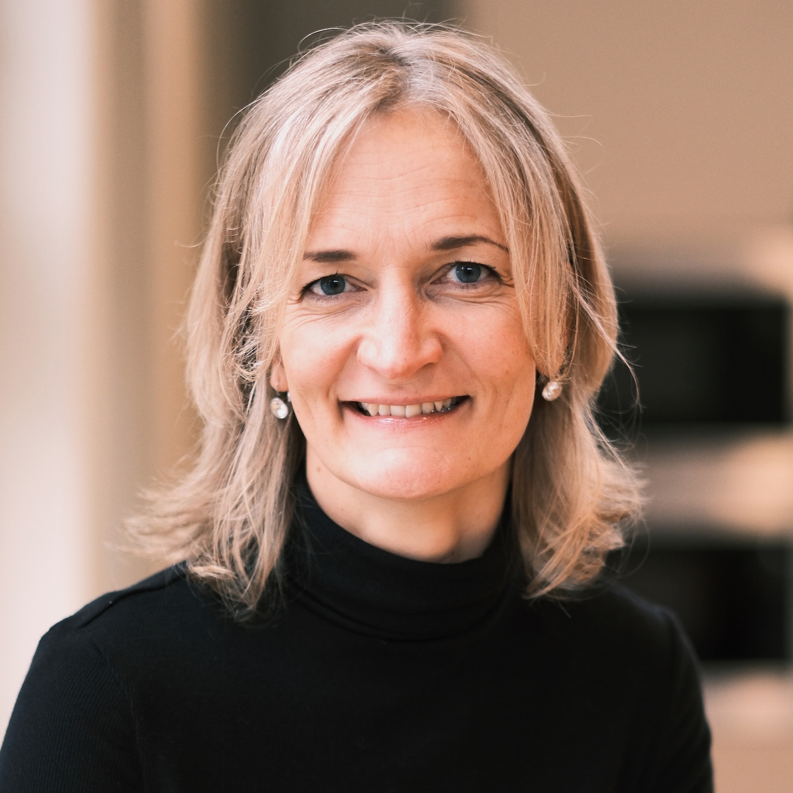 Foto på Unni Wihlborg, leendes med blont hår, silverörhängen och svart polotröja