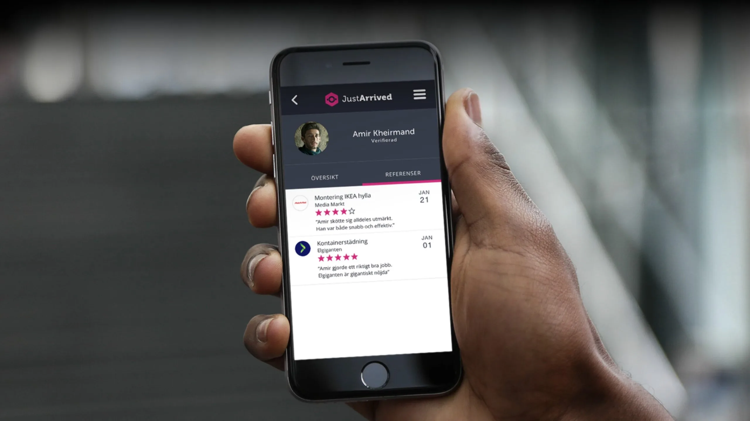 En hand håller i en mobil med appen JustArrived