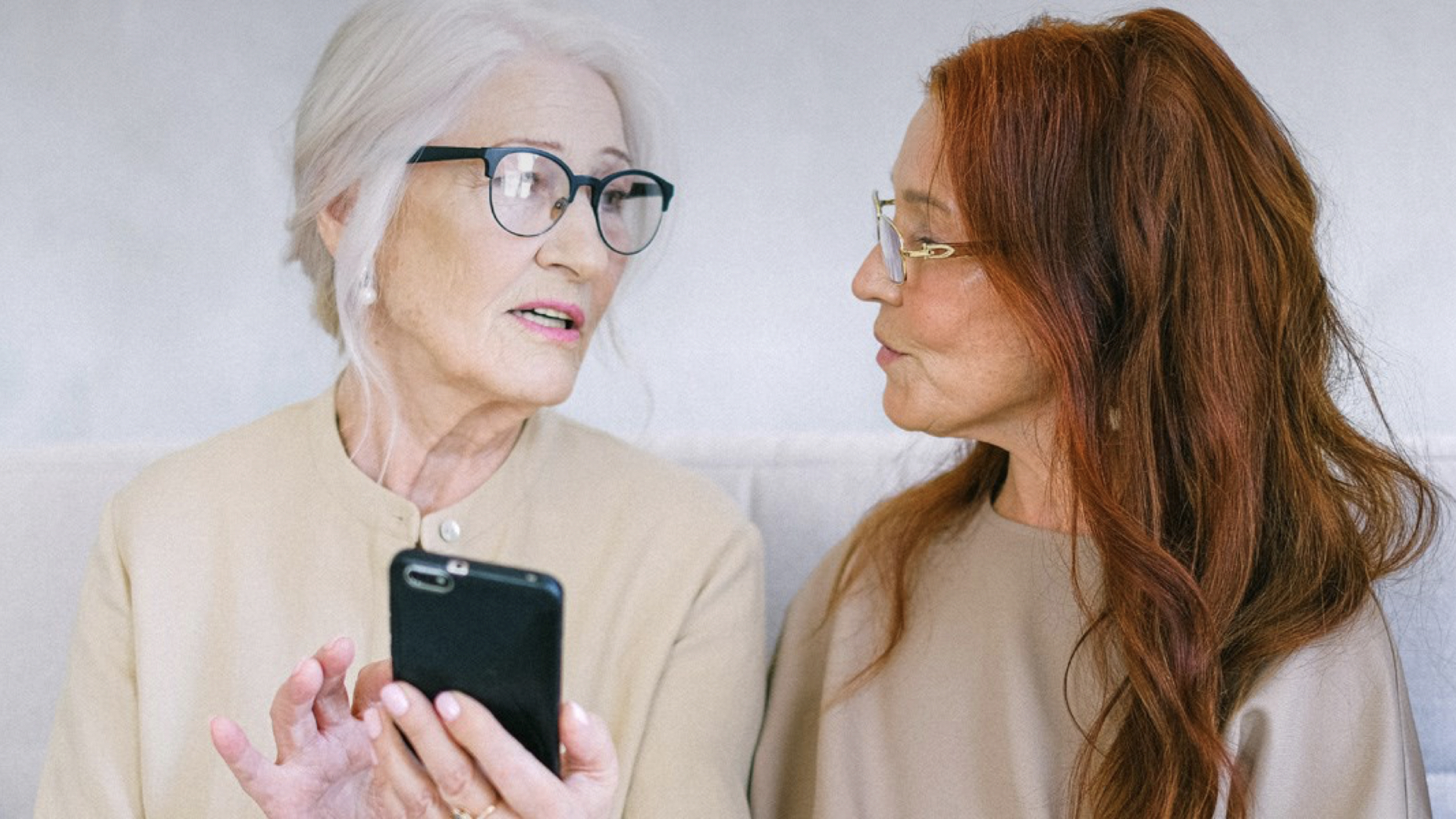 Två kvinnor samtalar med varandra. En av dem håller i en mobiltelefon.